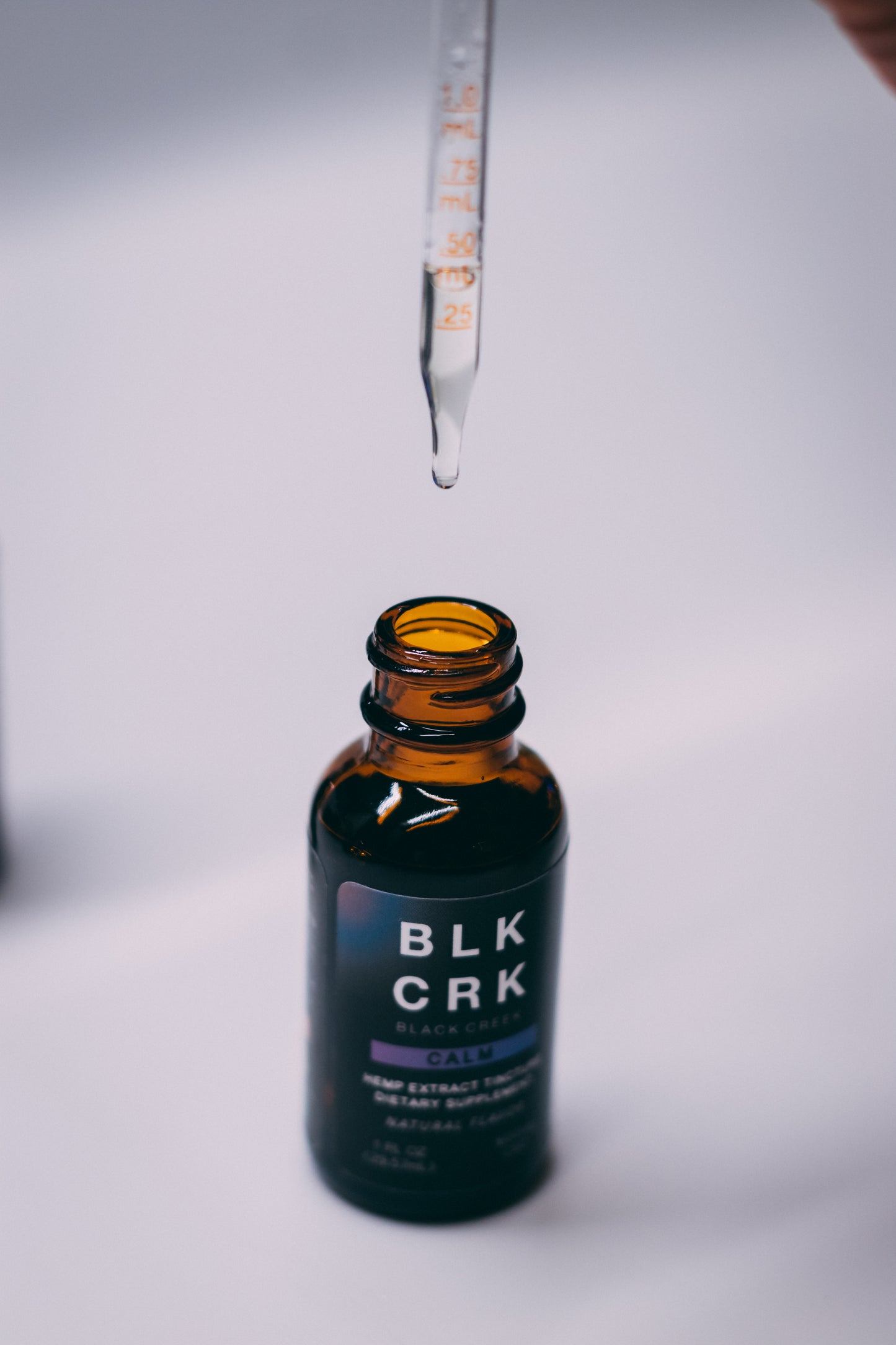 The Black Creek CBD Calm Tincture, 600 mg on a white background. The CBD tincture dropper is raised, with a drop of CBD oil about to drop back into the bottle