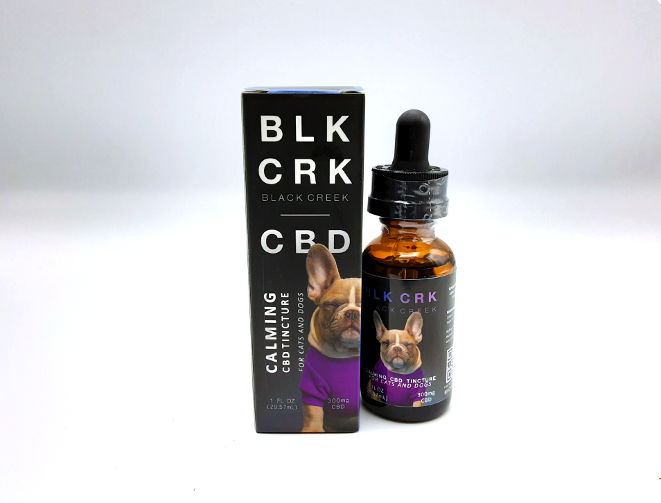 The Black Creek CBD Calming Pet Tincture with its box on a white background. A sleepy french bulldog in a purple shirt is on the front