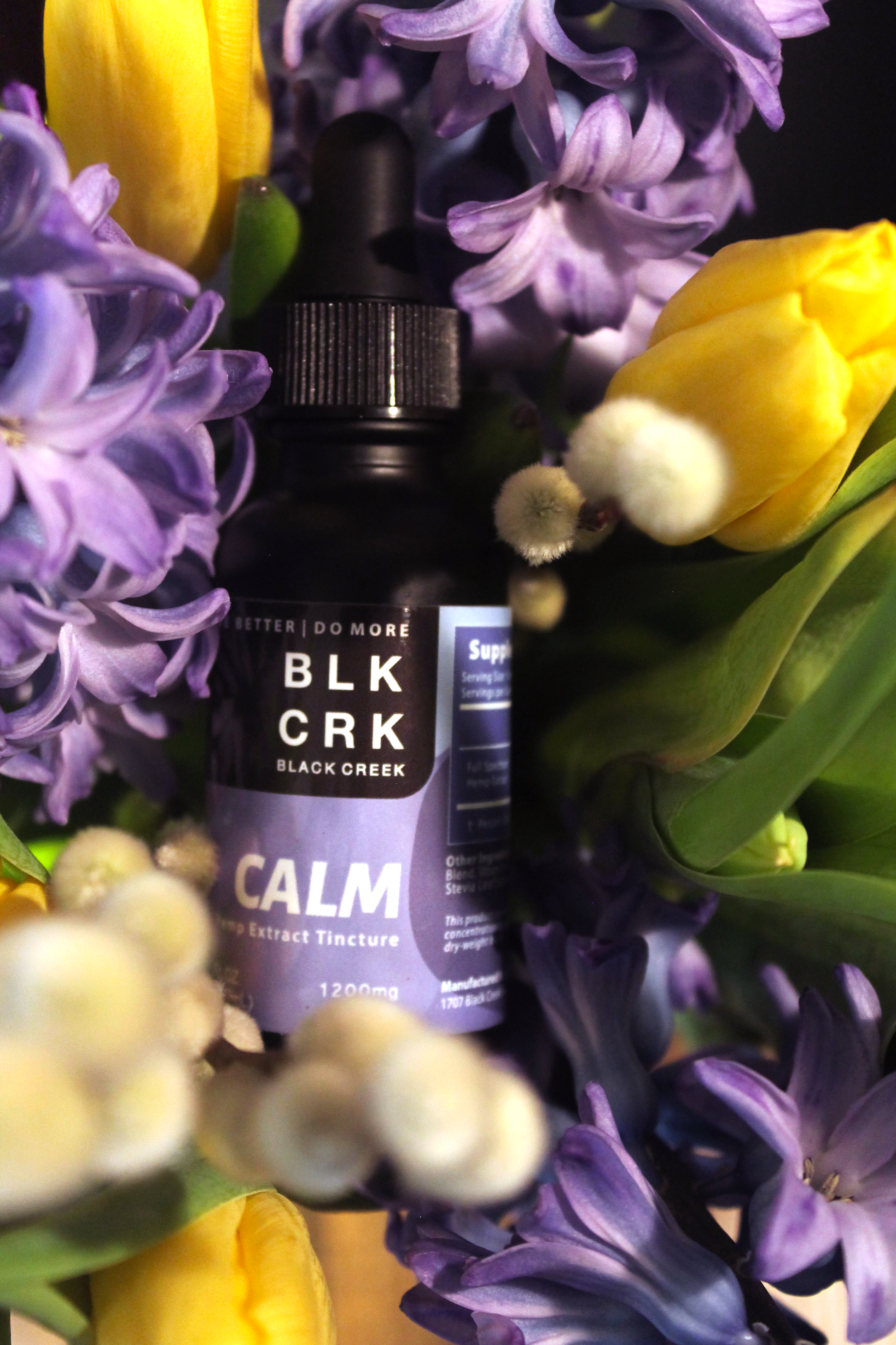 A Black Creek CBD Calm Tincture resting in a bouquet of purple , yellow, and white flowers