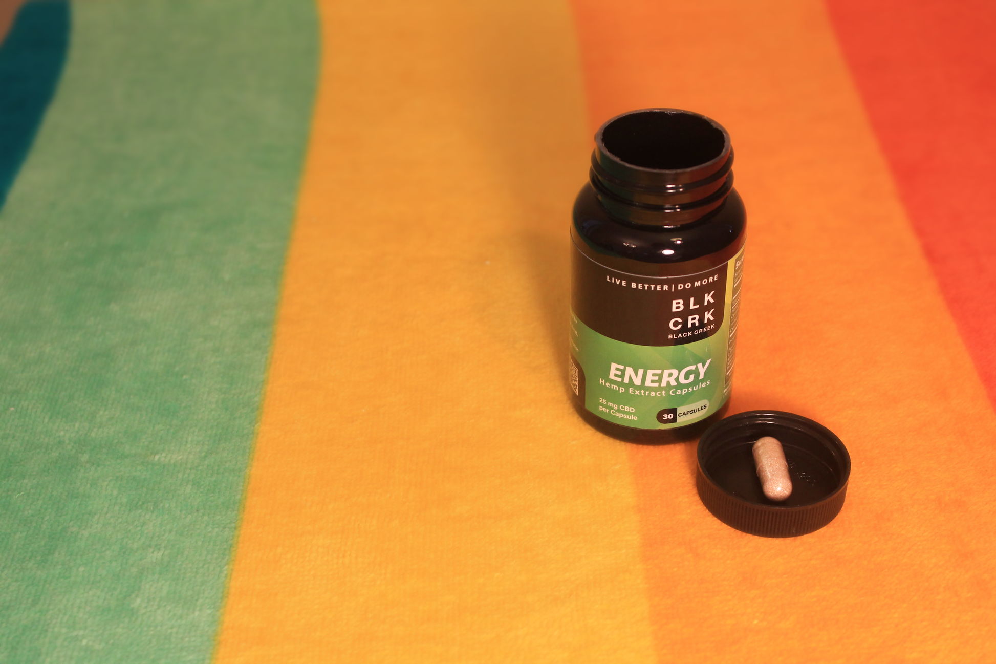 The Black Creek CBD Energy Capsules atop a colorful beach towel with one capsule sitting in the bottle's black cap
