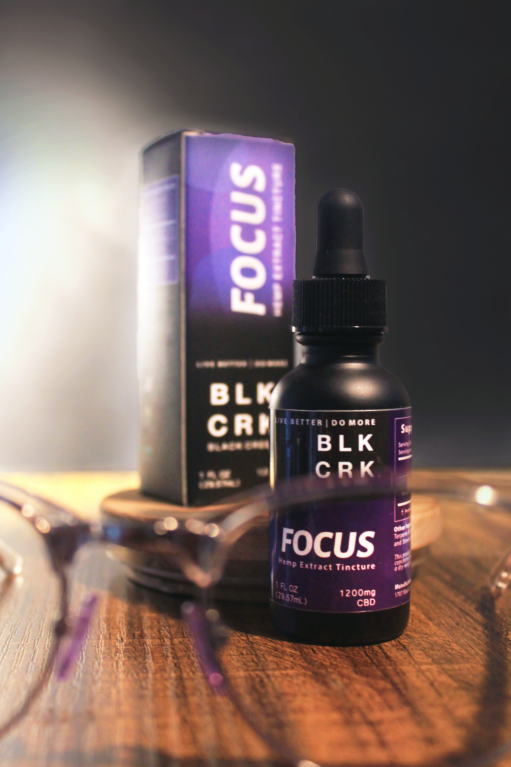 Black Creek CBD's Focus Tincture with a pair of glasses highlighting the word Focus. Standing on a wooden surface with a black background