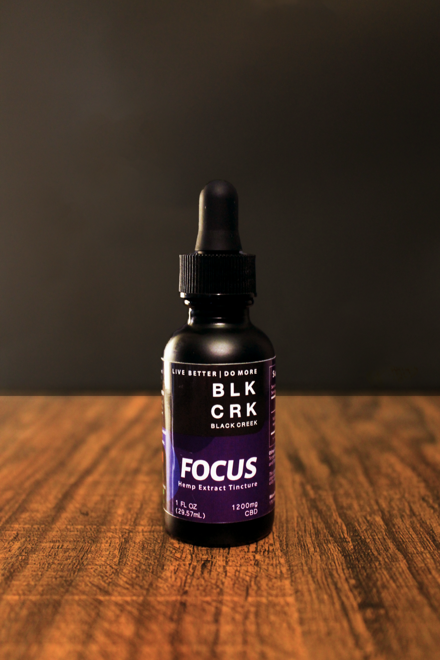 Black Creek CBD's Focus Tincture on a wood surface, black background. Purple and black CBD Tincture for Focus