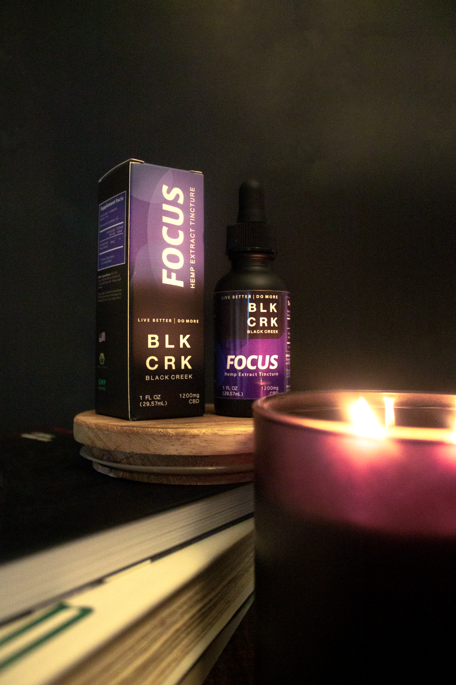 Black Creek CBD's Focus Tincture on a pile of books, sitting in front of a lit, black candle. 