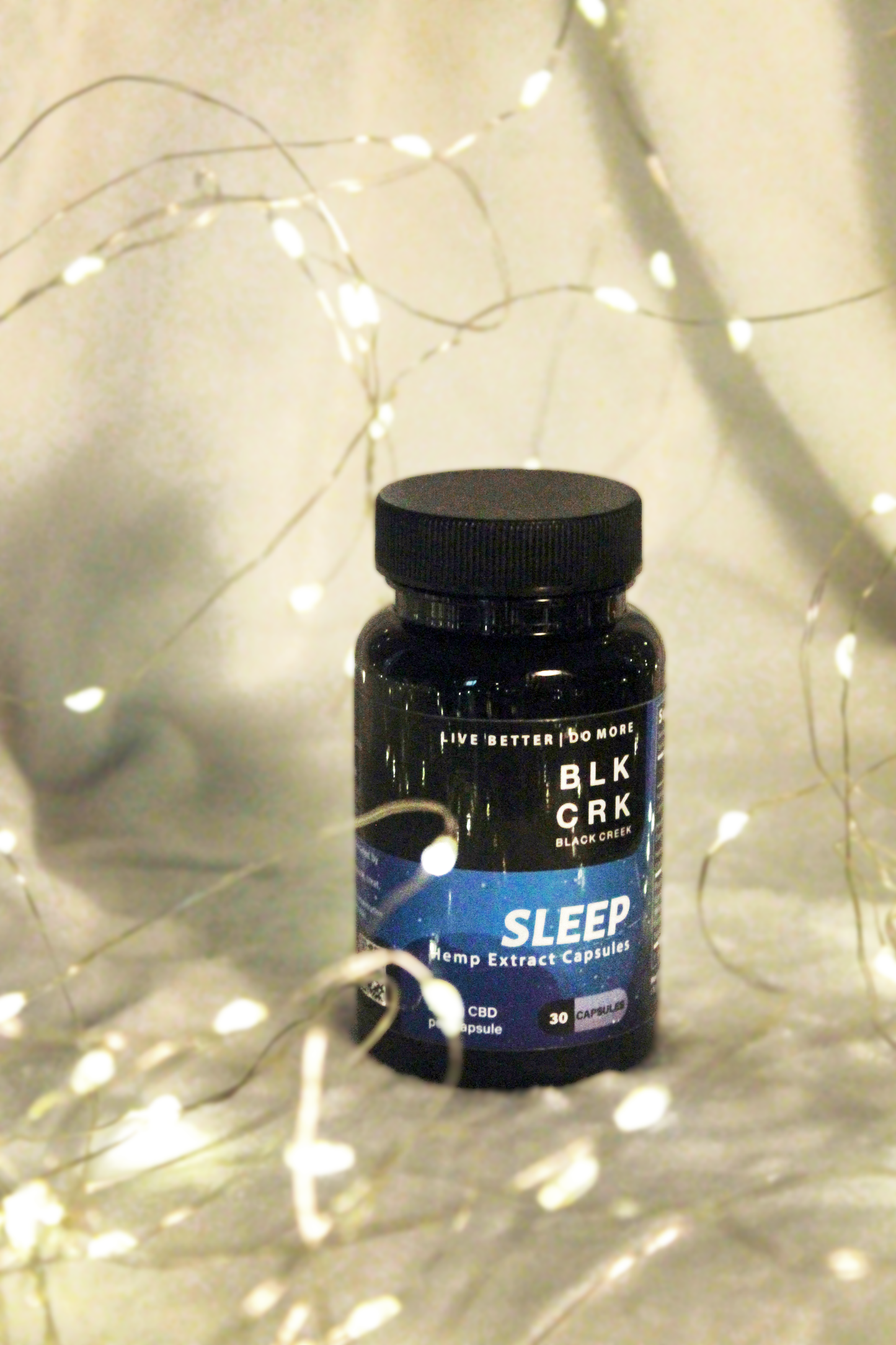 The Black Creek CBD Capsules on a white sheet with shiny fairy lights all around it